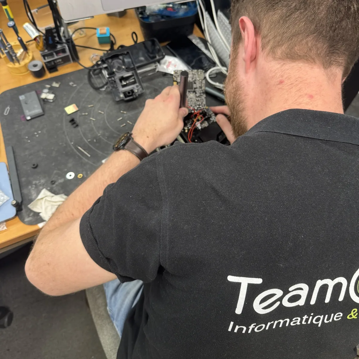 Technicien TeamClic penché sur une carte électronique, à l'atelier